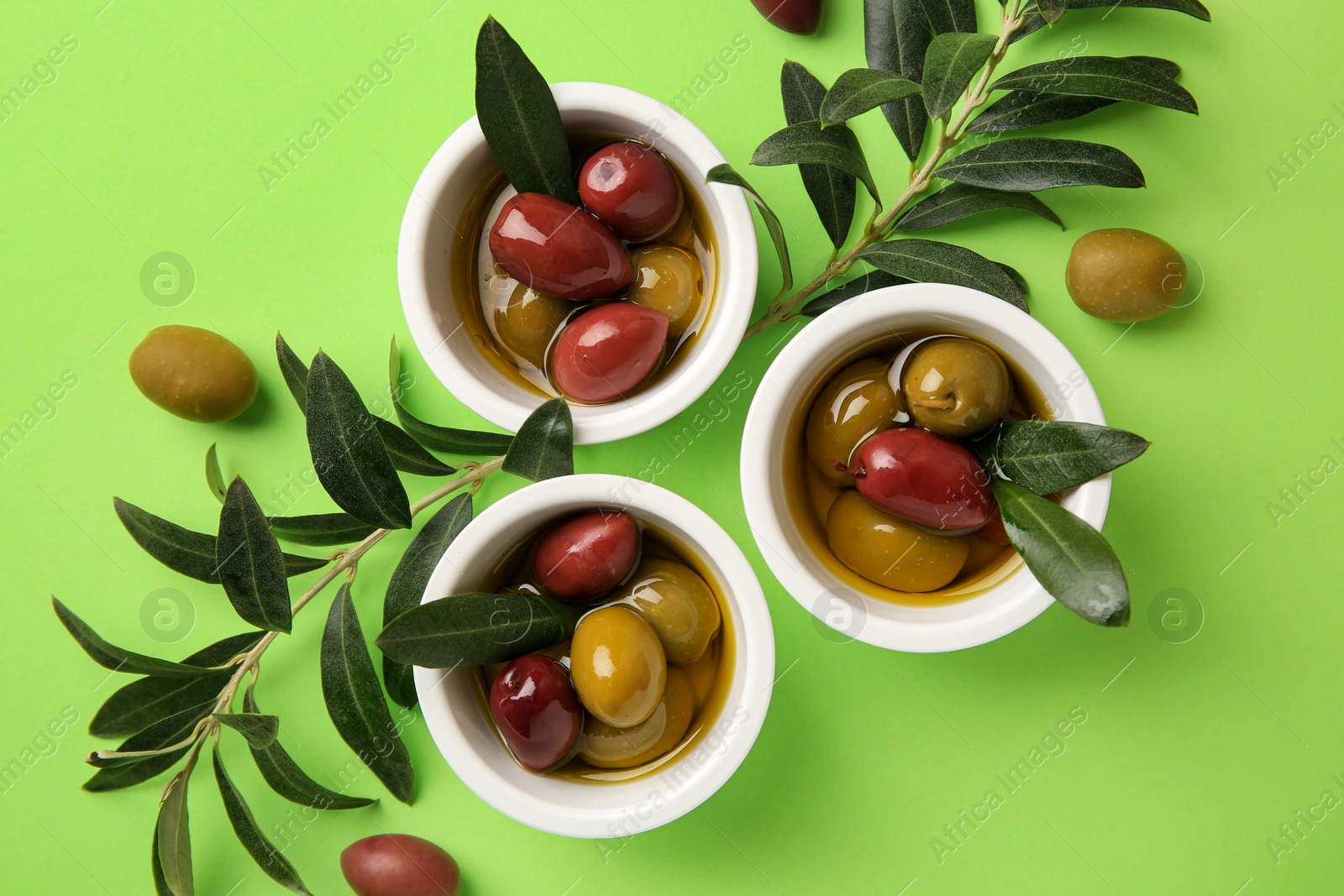 Photo of Bowls with different ripe olives and leaves on light green background, flat lay