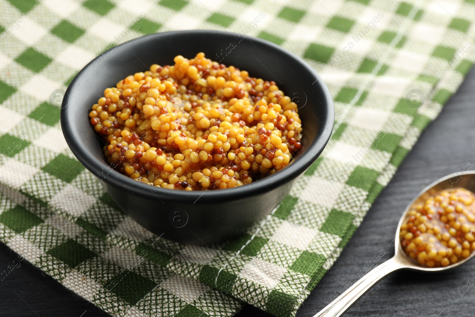 Photo of Bowl and spoon with whole grain mustard on black wooden table