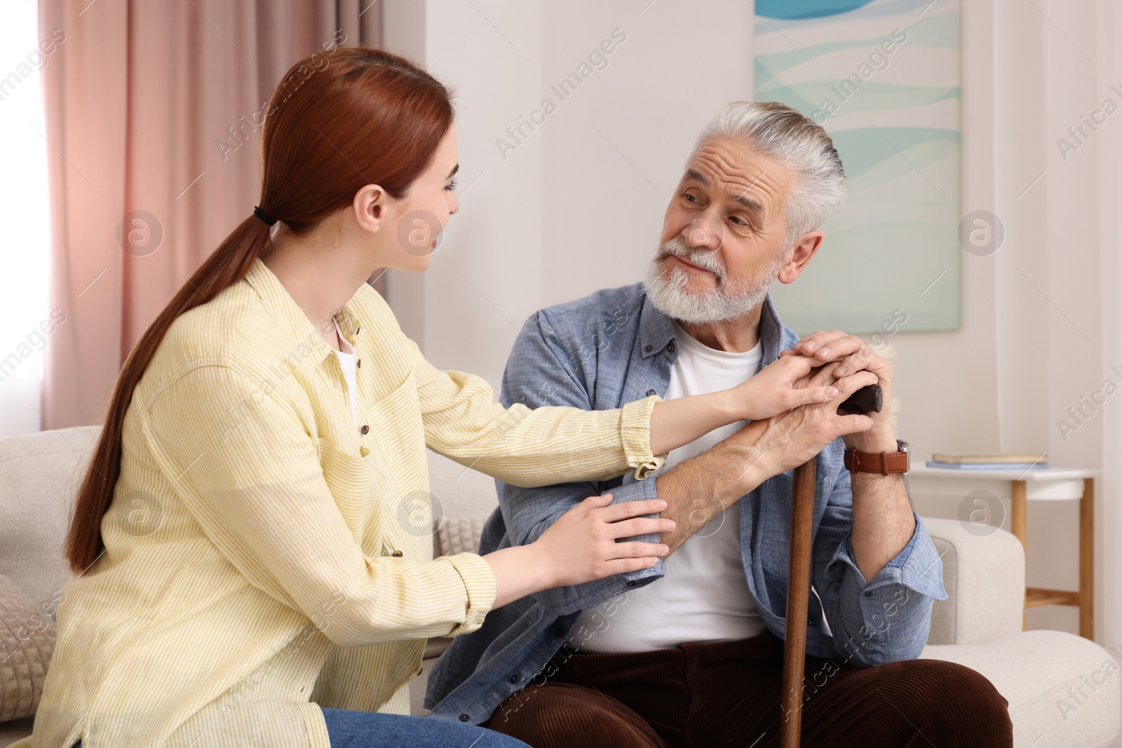 Photo of Caregiver and senior man with walking cane on sofa at home