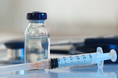 Photo of Glass vial, syringe and stethoscope on white table, closeup
