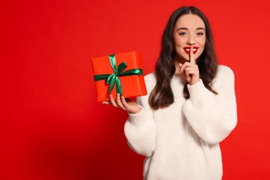 Photo of Beautiful young woman with Christmas gift on red background, space for text