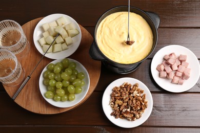 Photo of Fondue pot with tasty melted cheese, forks, wine and different snacks on wooden table, flat lay