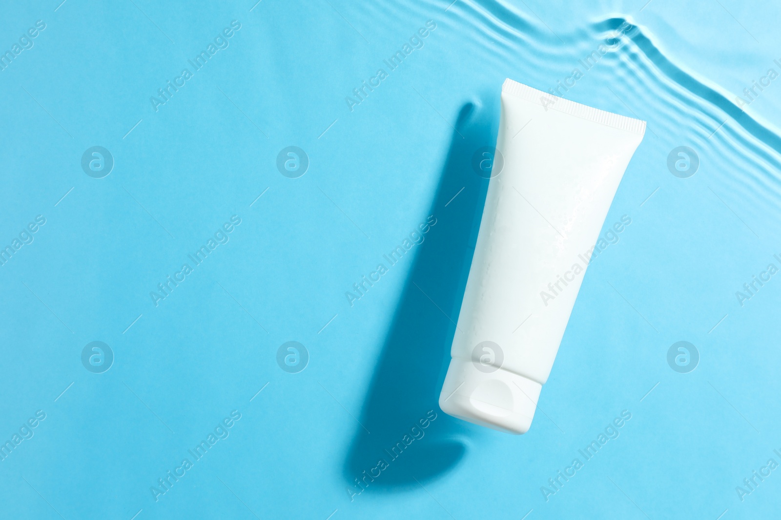 Photo of Tube with moisturizing cream in water on light blue background, top view. Space for text
