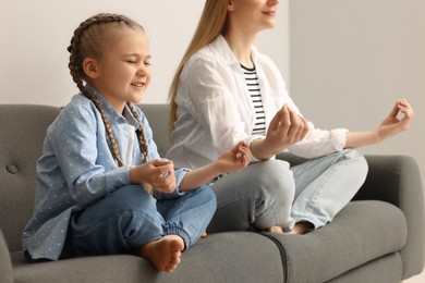 Photo of Mother with daughter meditating together on sofa indoors. Harmony and zen