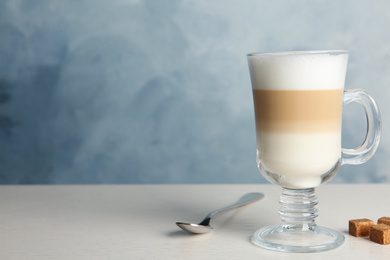 Delicious latte macchiato and sugar cubes on white table against light blue background, space for text