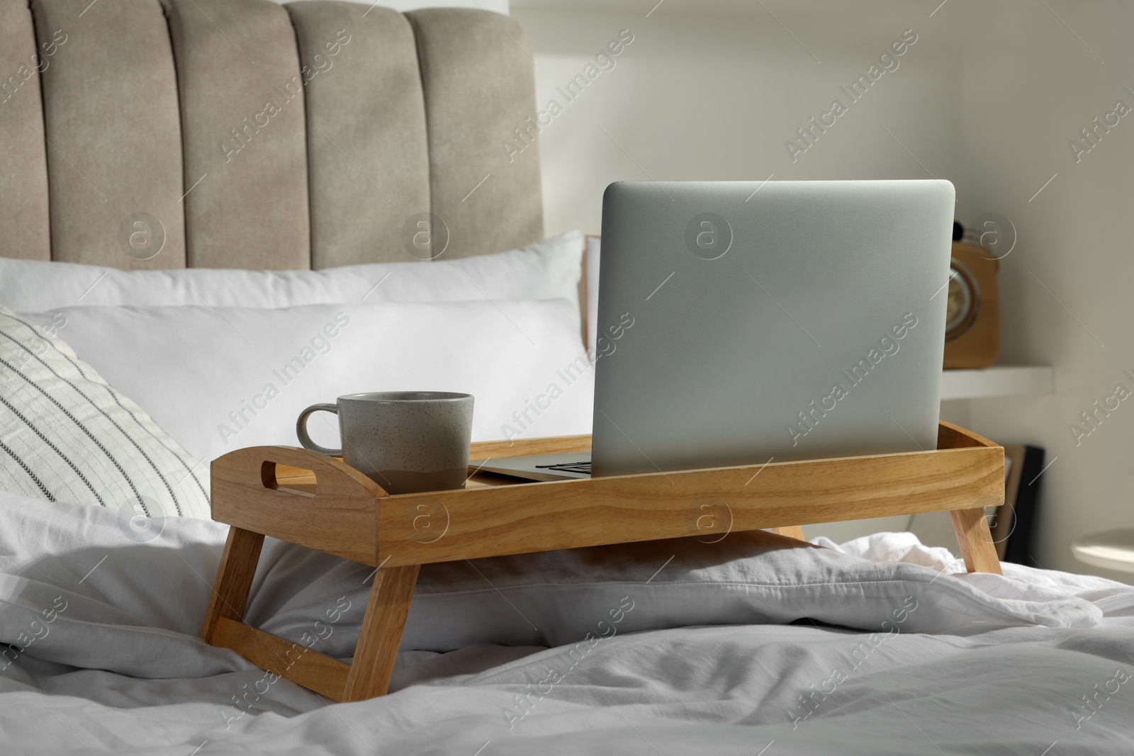 Photo of Wooden tray with modern laptop and cup of aromatic drink on bed indoors