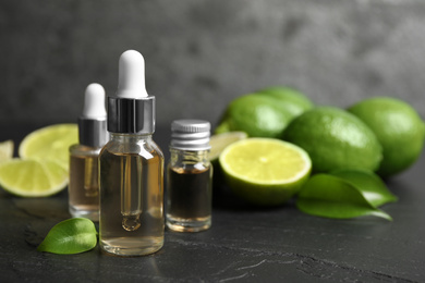 Photo of Lime essential oil and cut citrus fruits on black table