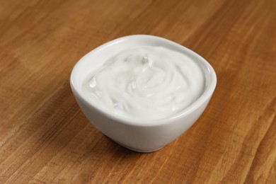 Photo of Bowl of tasty yogurt on wooden table