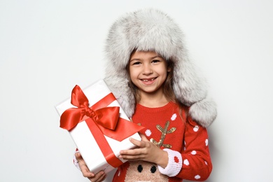 Photo of Cute little girl in Christmas sweater and hat holding gift on white background