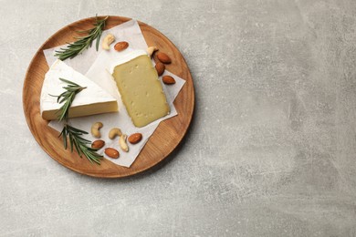 Photo of Plate with pieces of tasty camembert cheese, nuts and rosemary on grey textured table, top view. Space for text