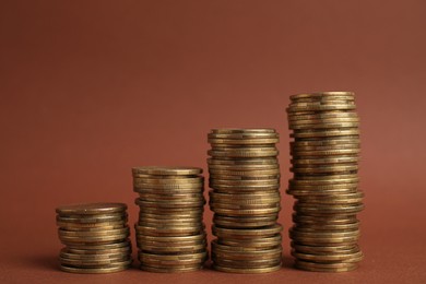 Many golden coins stacked on brown background, space for text