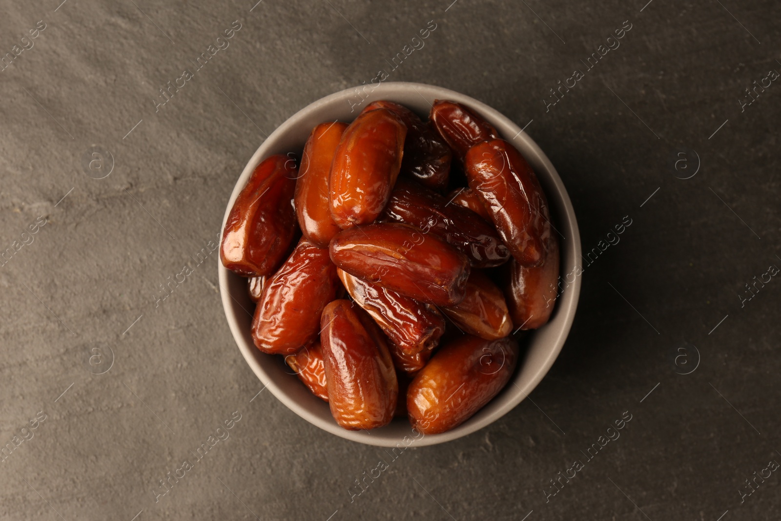 Photo of Tasty sweet dried dates in bowl on black table, top view