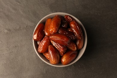 Photo of Tasty sweet dried dates in bowl on black table, top view