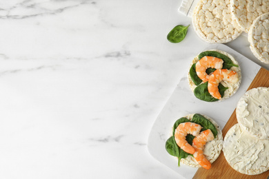 Photo of Puffed rice cakes with shrimps and basil on white marble table, flat lay. Space for text