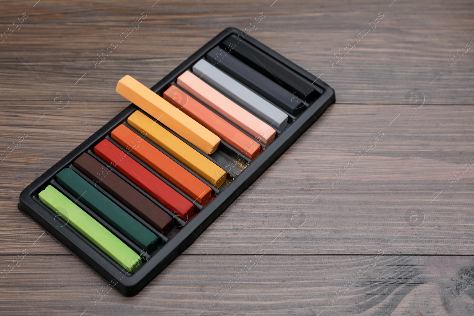 Photo of Colorful pastels in tray on wooden table, space for text. Drawing materials