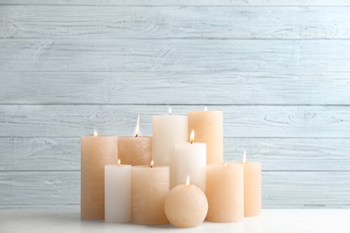 Set of burning candles on table against light wooden background