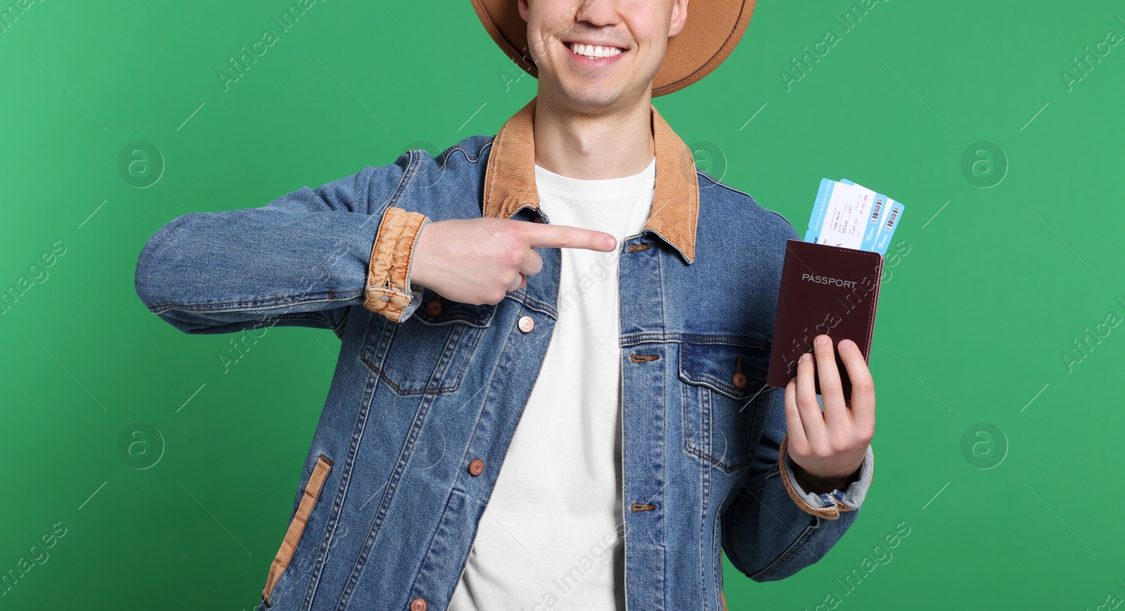 Photo of Smiling man pointing at passport and tickets on green background, closeup