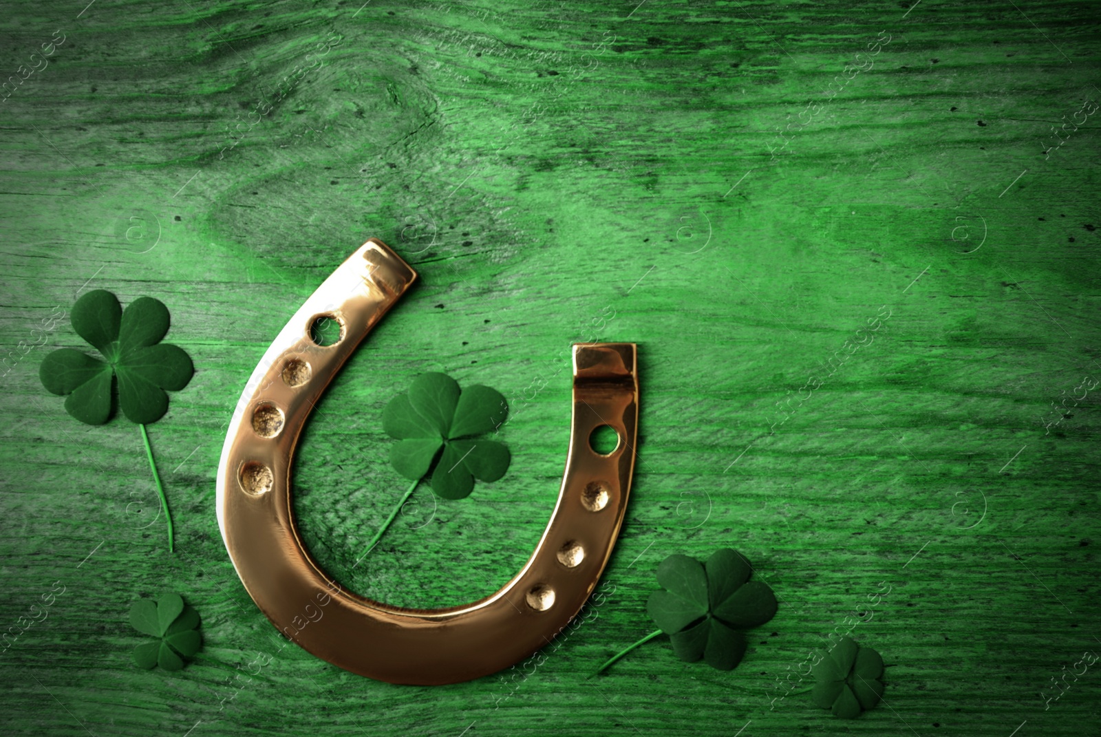 Image of Clover leaves and horseshoe on green wooden table, flat lay. St. Patrick's Day celebration