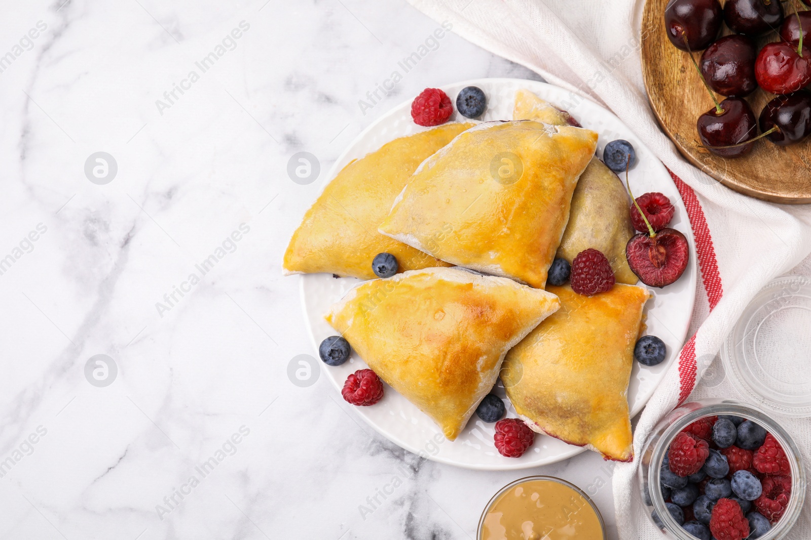 Photo of Delicious samosas with cherries and berries on white marble table, flat lay. Space for text