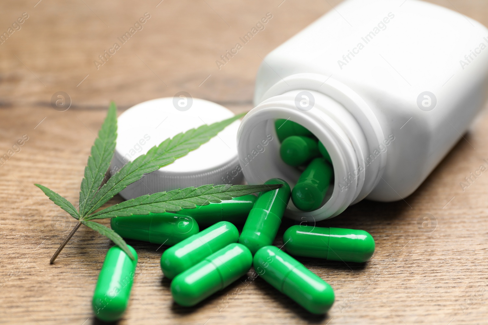 Photo of Hemp leaf and bottle with capsules on wooden table