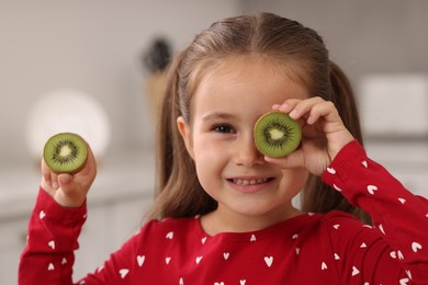 Photo of Cute little girl with fresh kiwi at home
