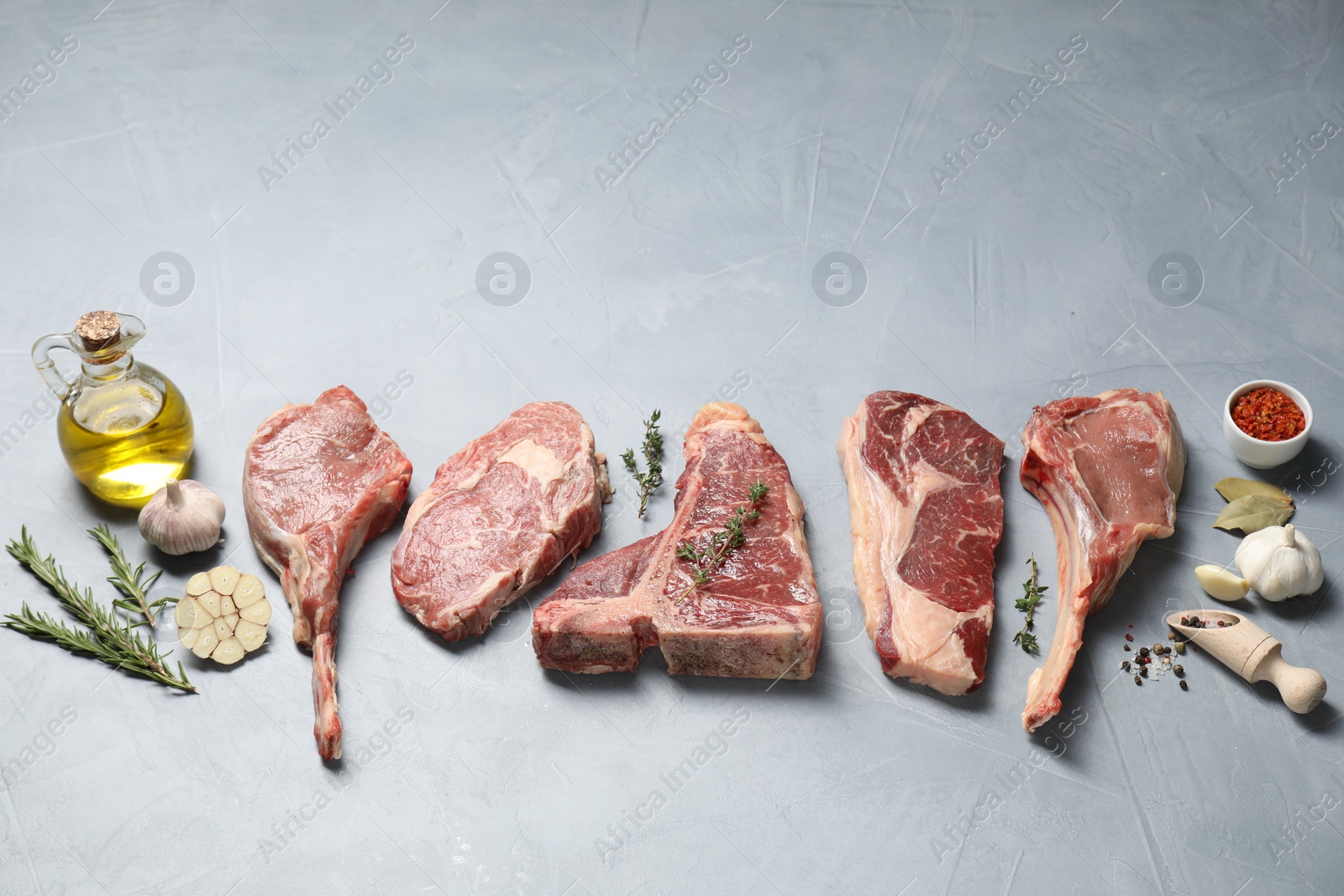 Photo of Fresh raw beef cuts, spices and oil on light grey textured table, above view. Space for text