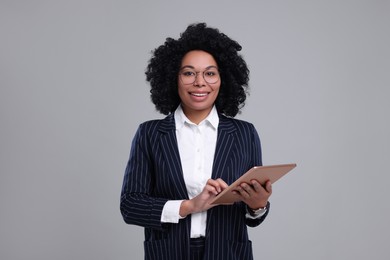 Young businesswoman with tablet on grey background