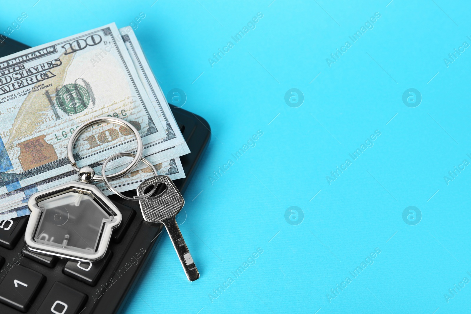 Photo of Key with trinket in shape of house, money and calculator on light blue background, space for text. Mortgage concept