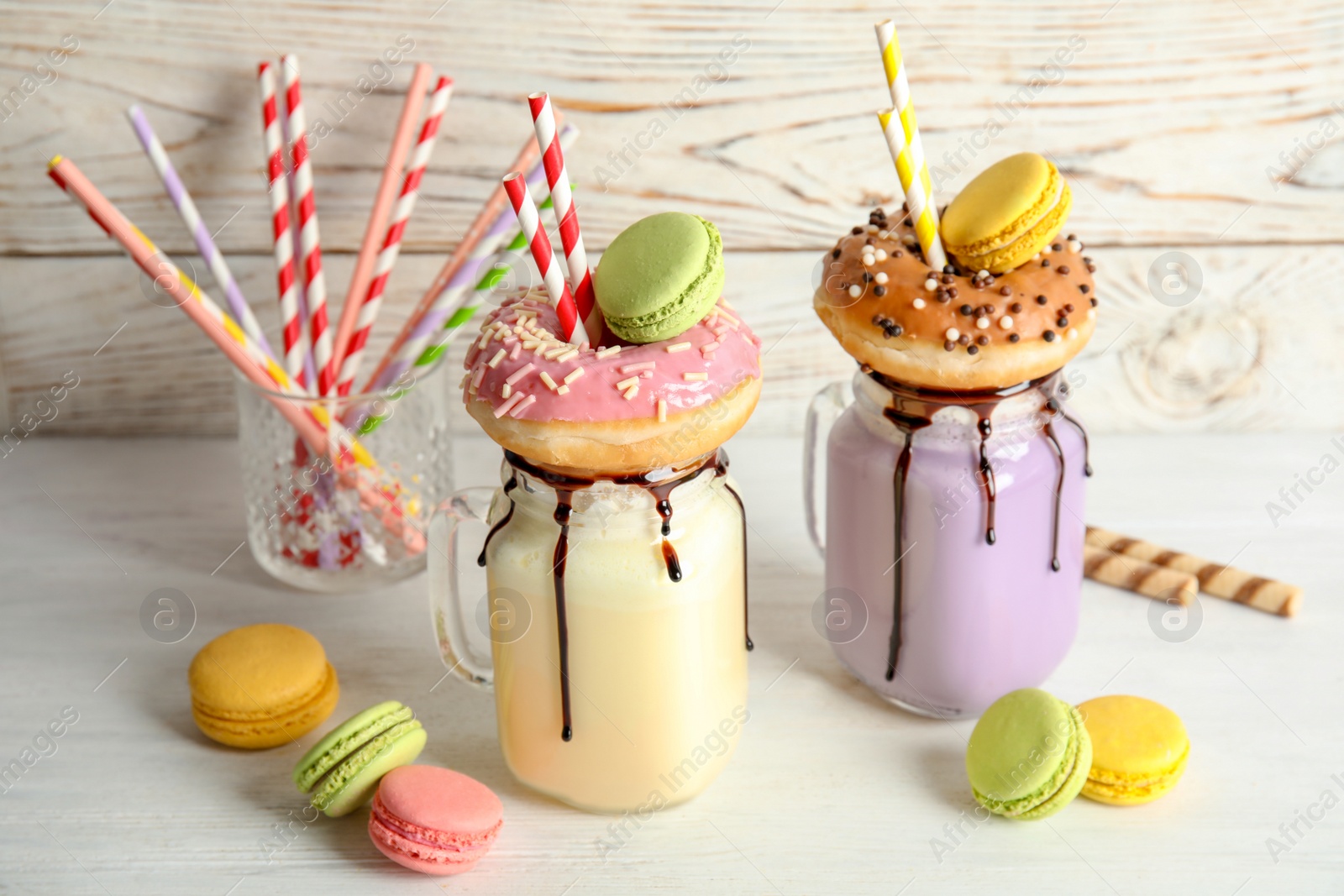 Photo of Mason jars with delicious milk shakes and macaroons on table