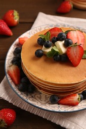 Photo of Delicious pancakes with fresh berries and butter served on wooden table, closeup