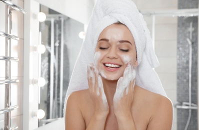 Young woman washing face with soap in bathroom