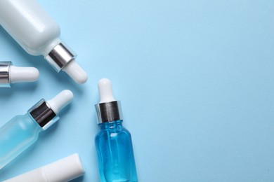 Photo of Many bottles and tube of cosmetic serum on light blue background, flat lay. Space for text