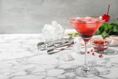 Glass of delicious cocktail with ice and cherry on white marble table. Space for text