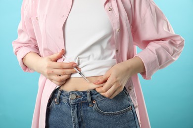 Diabetes. Woman making insulin injection into her belly on light blue background, closeup