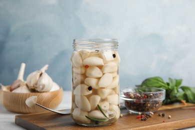 Photo of Composition with jar of pickled garlic on white table against blue background