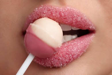 Photo of Young woman with beautiful lips covered in sugar eating lollipop, closeup