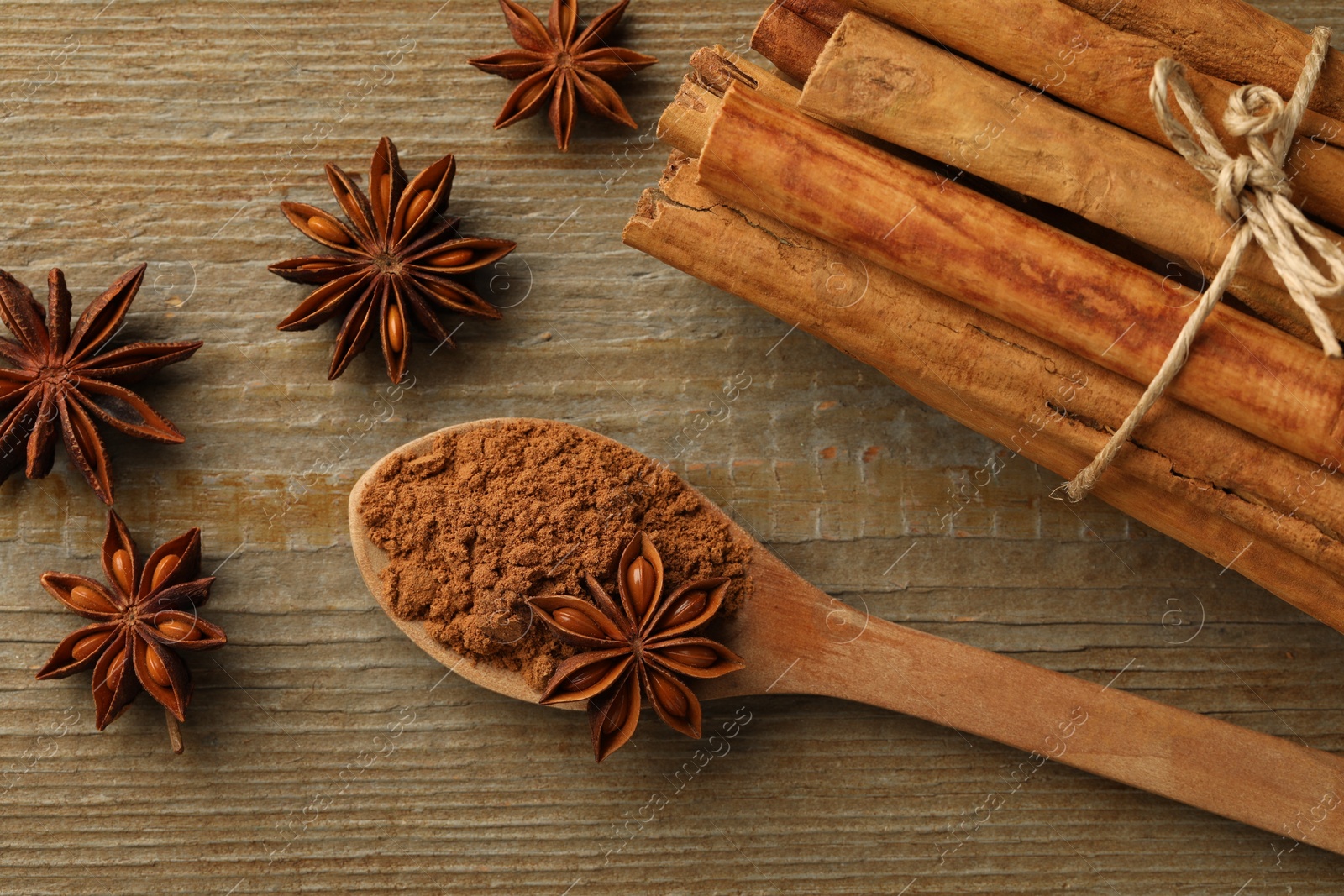 Photo of Spoon with cinnamon powder, sticks and star anise on wooden table, flat lay