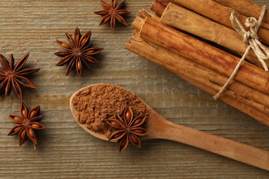 Spoon with cinnamon powder, sticks and star anise on wooden table, flat lay