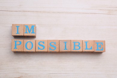 Photo of Motivation concept. Changing word from Impossible into Possible by removing cubes on light wooden table, flat lay
