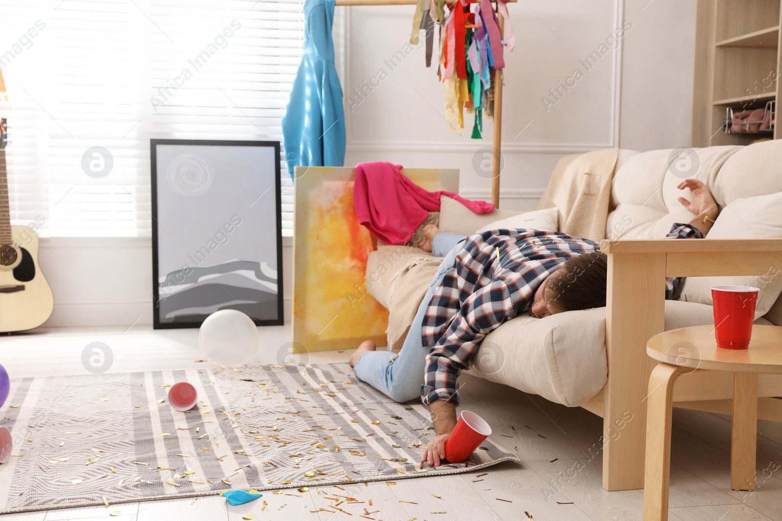 Photo of Young man sleeping on sofa in messy room after party