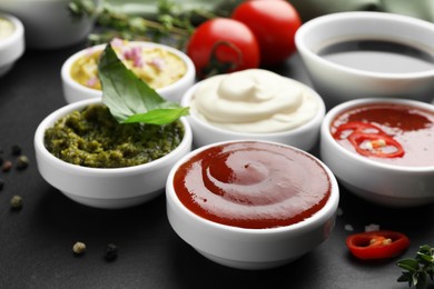 Different tasty sauces in bowls and ingredients on black table, closeup