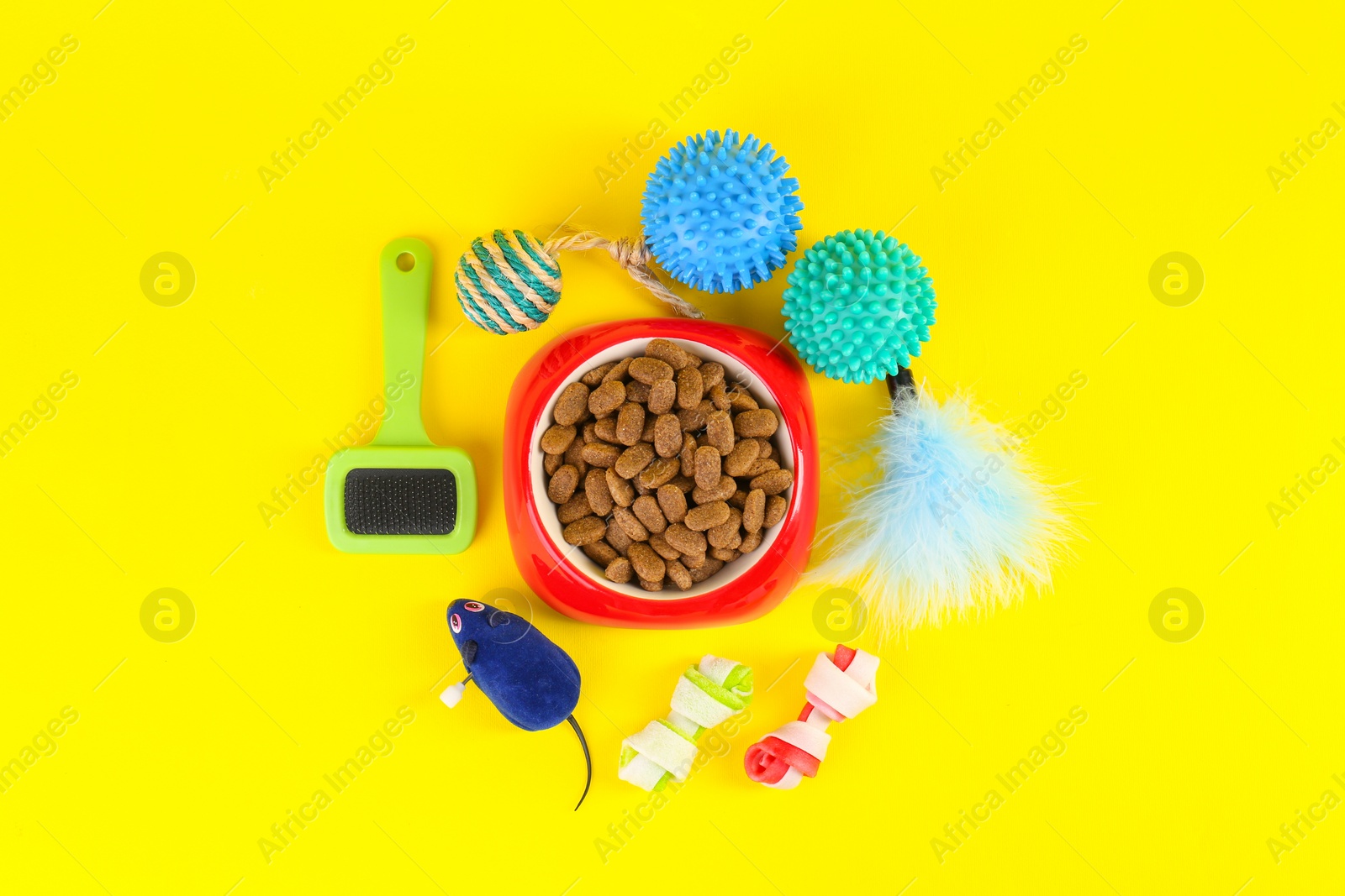 Photo of Bowl of dry food, brush and toys on yellow background, flat lay. Pet shop goods