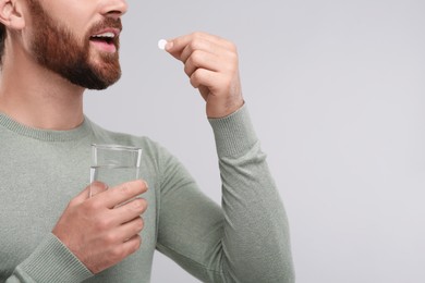 Photo of Man with glass of water taking pill on light grey background, closeup. Space for text