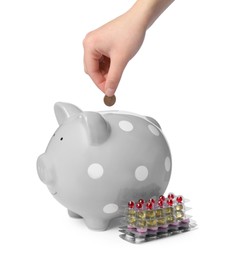 Photo of Woman putting coin into piggy bank and pills on white background, closeup. Medical insurance