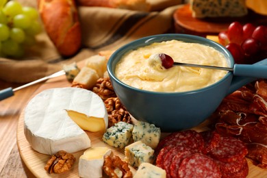 Fondue pot with tasty melted cheese, forks and different snacks on table