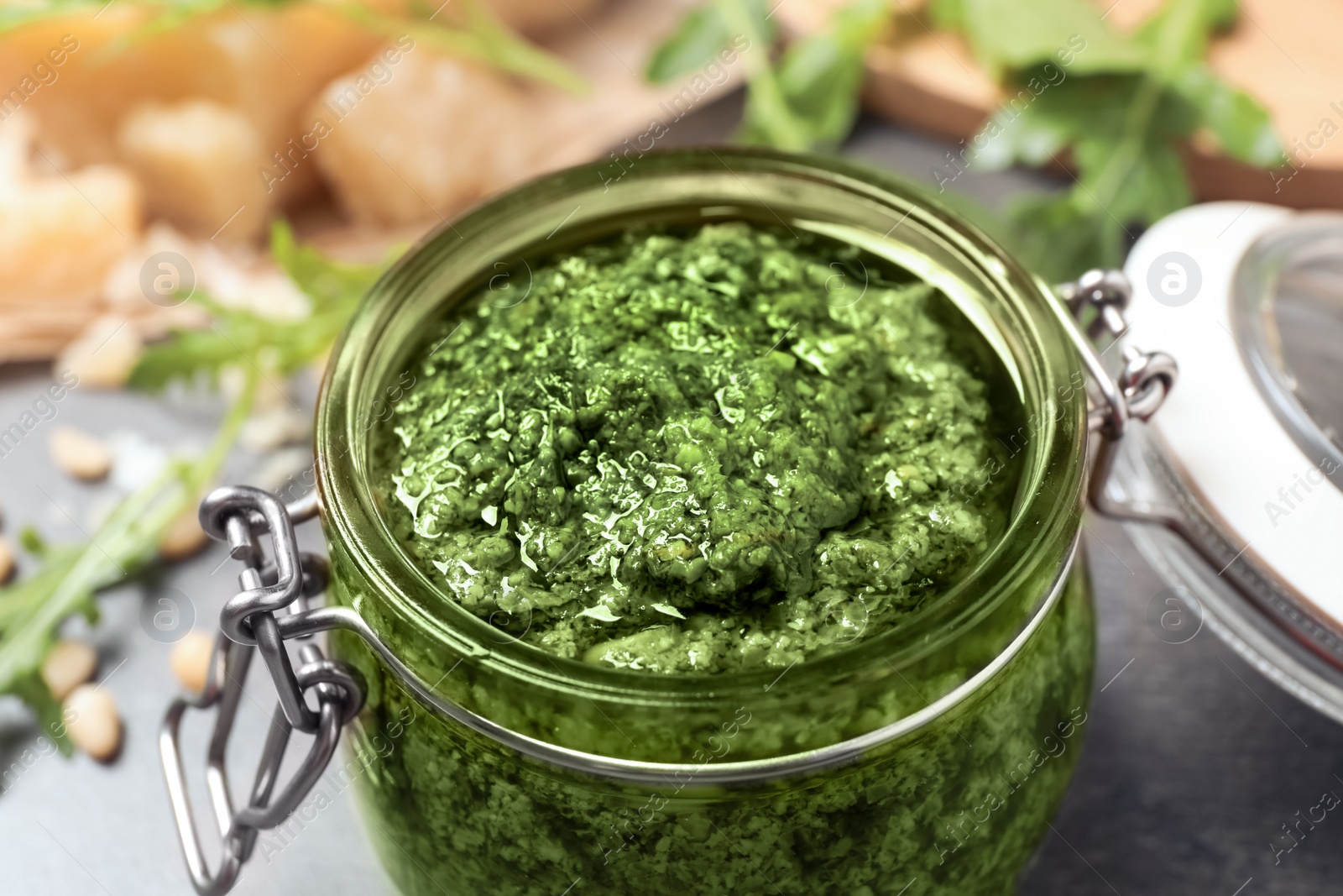 Photo of Jar of tasty arugula pesto on table, closeup