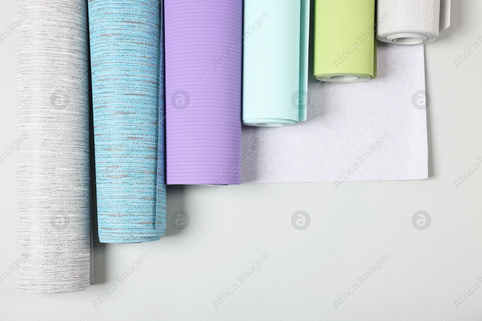 Photo of Different wallpaper rolls on light background, flat lay. Space for text