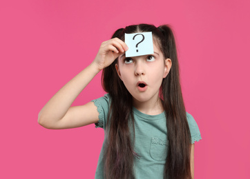 Photo of Emotional girl with question mark sticker on forehead against pink background