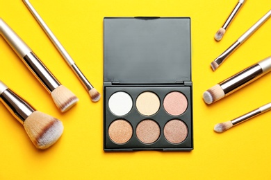 Photo of Flat lay composition with professional makeup brushes and eye shadow palette on yellow background