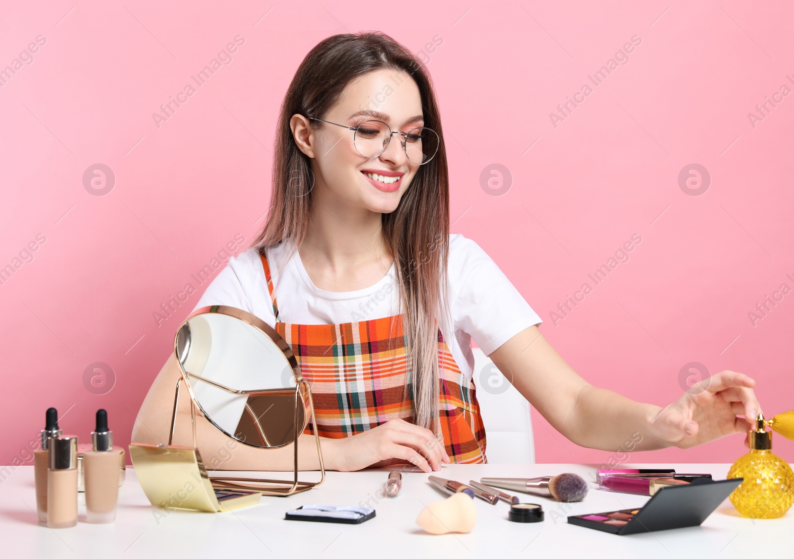 Photo of Beauty blogger at table with different cosmetic products against pink background